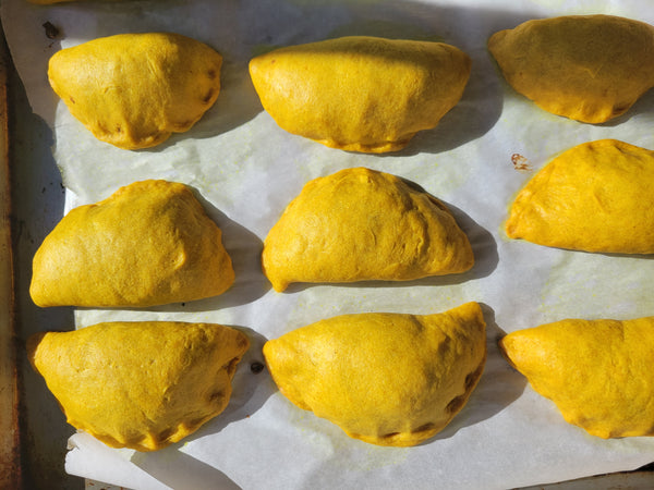 Nine uncooked golden Jamaican patties arranged on a baking sheet lined with parchment paper.