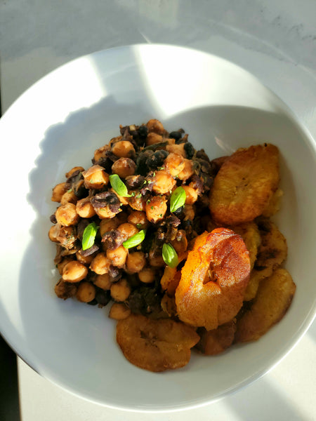 A white bowl of Jerk Peas cooked with Cole's Kitchen Organic Jerk Marinade, served with fried sweet plantains and garnished with fresh green herbs.