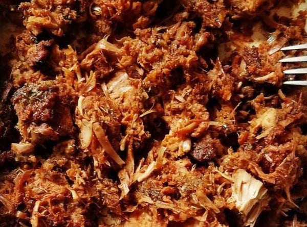 Close-up of shredded pulled meat coated in a rich, dark Cole's Kitchen Organic Jerk Marinade, showing the juicy texture and spice infusion.