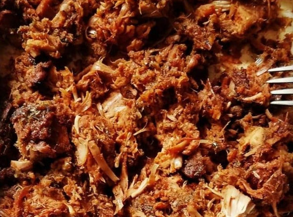 A close-up of tender shredded meat seasoned with Cole's Kitchen Organic Jerk Spice Rub, showing the rich mahogany color and herb-flecked texture of the Caribbean seasoning