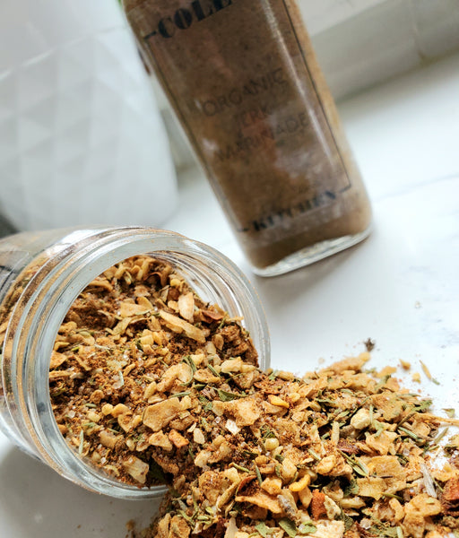 An overhead view of an open jar of Cole's Kitchen Organic Jerk Spice Rub, showing the rich texture of dried onion, garlic, and Caribbean herbs.
