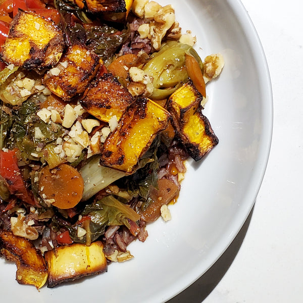 A roasted vegetable medley featuring squash, carrots, and leafy greens seasoned with Cole's Kitchen Veggie Cure Spice Blend, topped with chopped walnuts and served over red rice.