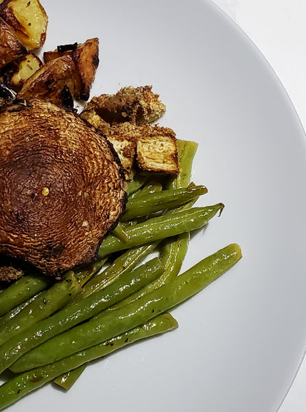 A close-up of roasted mushroom and seasoned green beans on a white plate, prepared with Cole's Kitchen Veggie Cure Spice Blend for a healthy side dish.