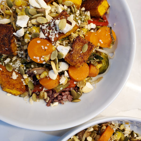 A colorful roasted vegetable bowl with carrots, Brussels sprouts, and pumpkin seeds seasoned with Cole's Kitchen Veggie Cure Spice Blend, served over a bed of wild rice.