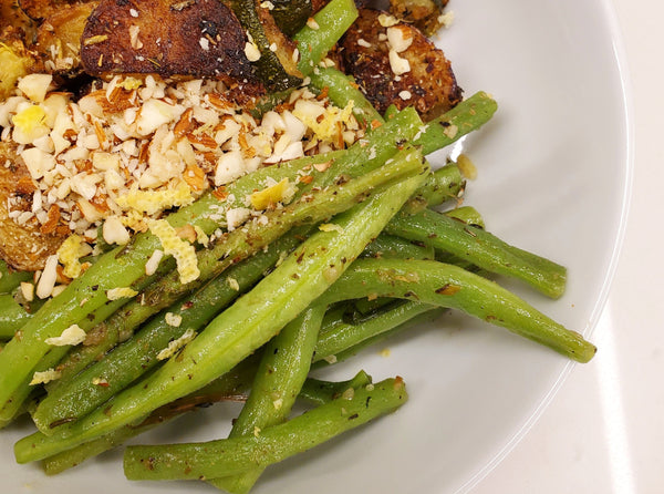 Sautéed fresh green beans seasoned with Cole's Kitchen Veggie Cure Spice Blend, topped with toasted breadcrumbs and garlic on a white plate.