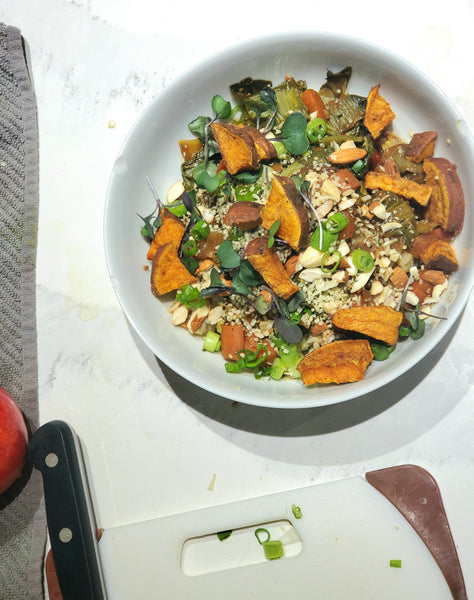 A nutritious grain bowl featuring roasted sweet potatoes, greens, and seeds seasoned with Cole's Kitchen Veggie Cure Spice Blend, shown on a kitchen counter next to a cutting board.